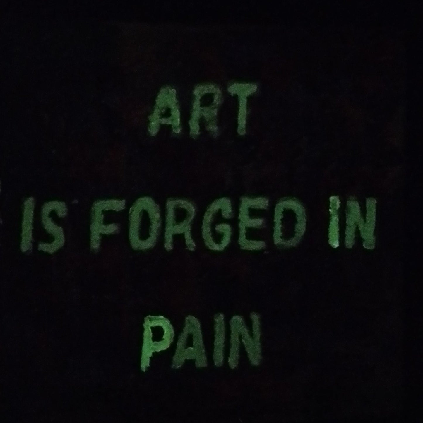 “Glow in the dark expressionist painting with quote ‘Art Is Forged in Pain’ illuminated at night.”