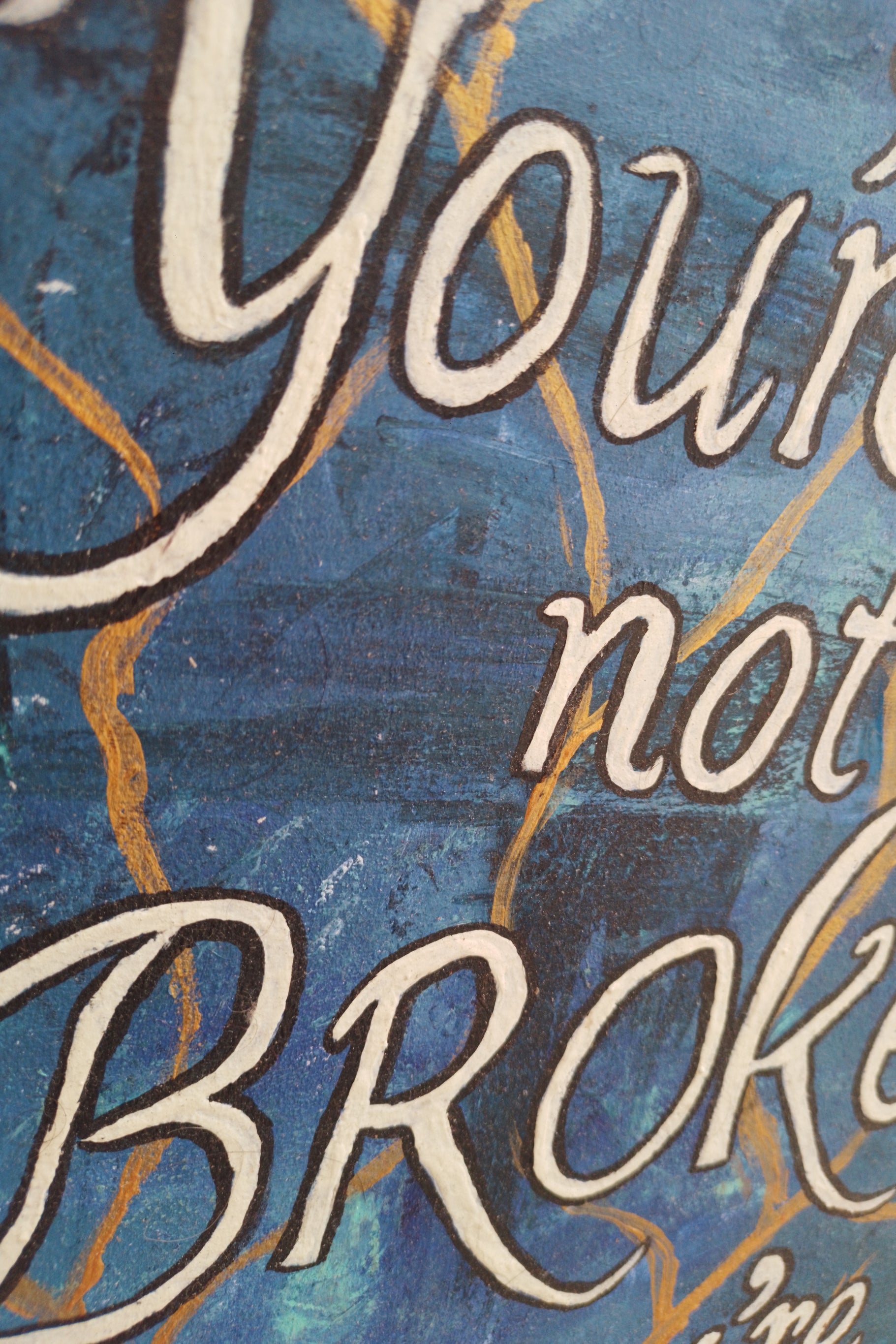 “Close-up detail of textured brushstrokes and golden crack lines on painting with quote: ‘You’re not broken, you’re becoming."